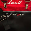 Close-up of J'adore red apron featuring embroidered text 'Love it!' and stylish adjustable straps.