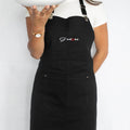 J'adore black cooking apron worn by woman, featuring adjustable straps and deep front pocket, perfect for culinary enthusiasts.