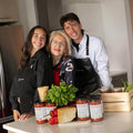 Three people in a kitchen wearing aprons, surrounded by fresh ingredients and jars, promoting culinary tradition and family.